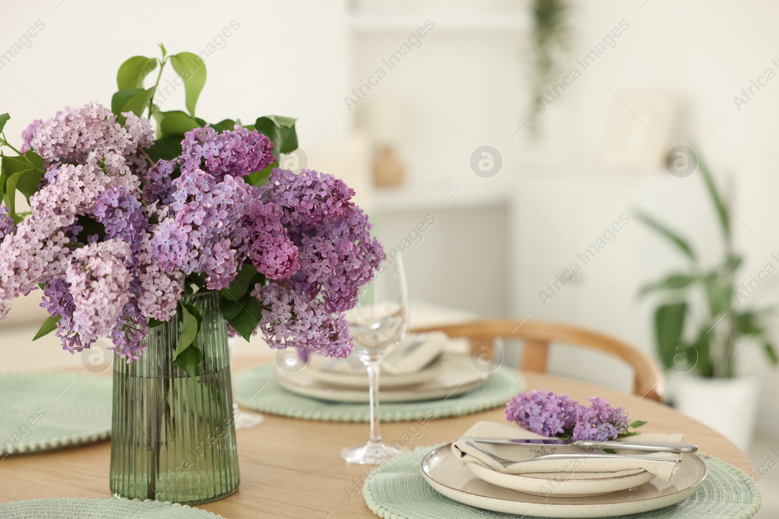 Beautiful lilac flowers, plates, cutlery and glass on wooden table indoors Photo of Beautiful lilac flowers, plates, cutlery and glass on wooden table indoors