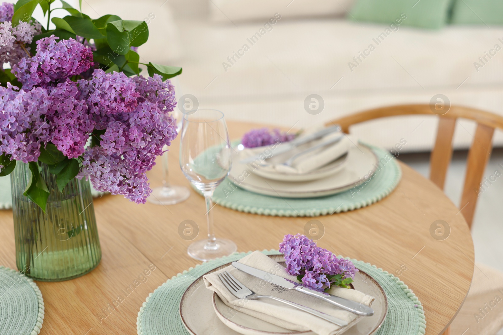 Beautiful lilac flowers, plates, cutlery and glasses on wooden table indoors Photo of Beautiful lilac flowers, plates, cutlery and glasses on wooden table indoors