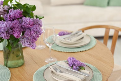Photo of Beautiful lilac flowers, plates, cutlery and glasses on wooden table indoors