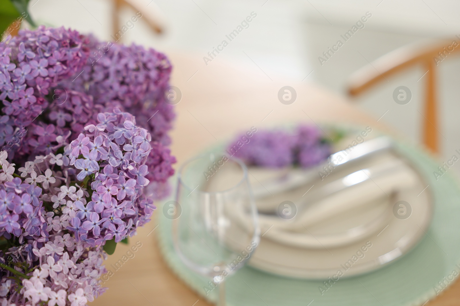 Beautiful lilac flowers, plates, cutlery and glass on table, closeup. Space for text Photo of Beautiful lilac flowers, plates, cutlery and glass on table, closeup. Space for text