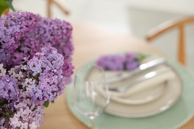 Photo of Beautiful lilac flowers, plates, cutlery and glass on table, closeup. Space for text