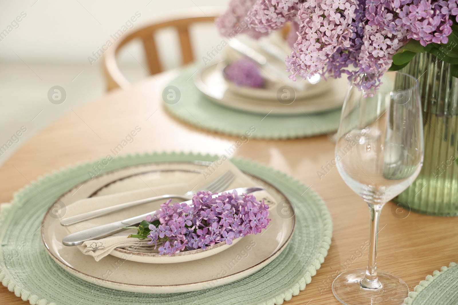 Beautiful lilac flowers, plates, cutlery and glass on wooden table indoors, closeup Photo of Beautiful lilac flowers, plates, cutlery and glass on wooden table indoors, closeup