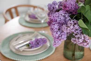 Photo of Beautiful lilac flowers, plates, cutlery and glass on table indoors, closeup