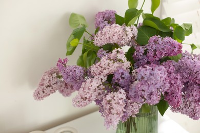 Photo of Beautiful lilac flowers in vase on table indoors, closeup