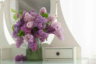 Photo of Beautiful lilac flowers in vase on dressing table indoors
