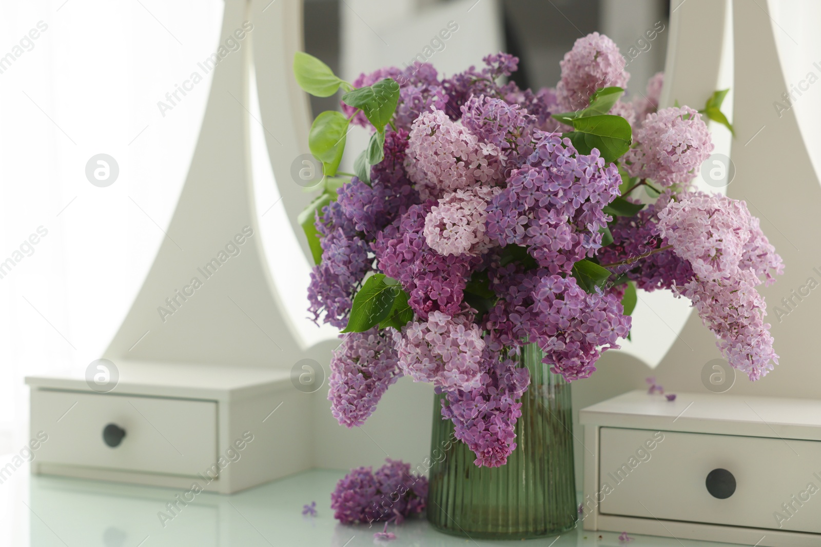 Beautiful lilac flowers in vase on dressing table indoors Photo of Beautiful lilac flowers in vase on dressing table indoors