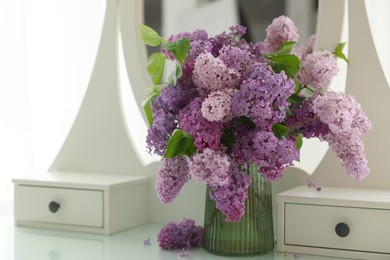 Photo of Beautiful lilac flowers in vase on dressing table indoors