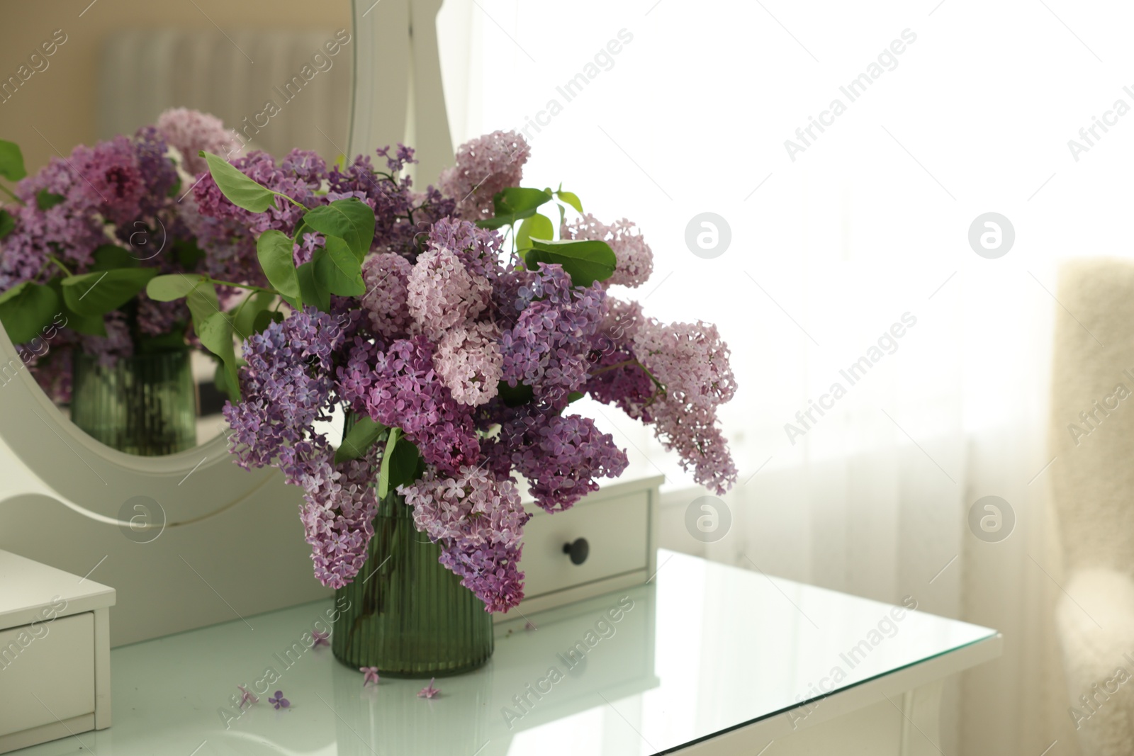 Beautiful lilac flowers in vase on dressing table indoors, space for text Photo of Beautiful lilac flowers in vase on dressing table indoors, space for text