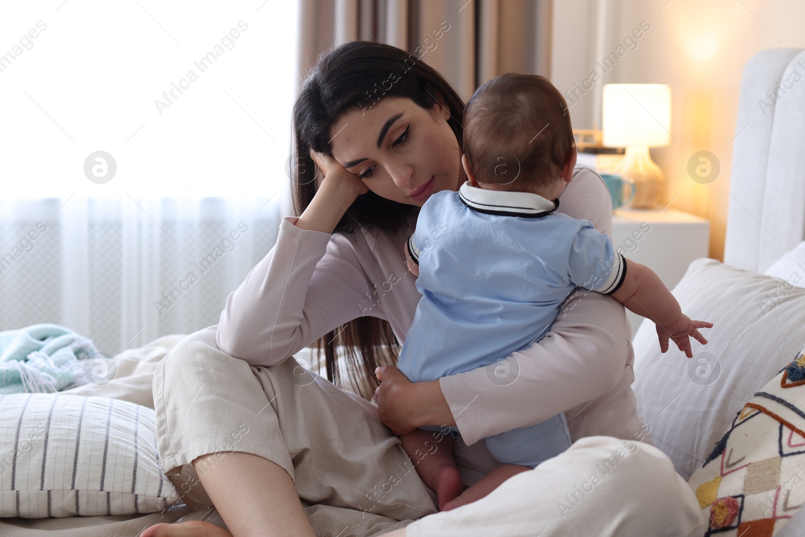 Woman suffering from postpartum depression with her little baby on bed at home Photo of Woman suffering from postpartum depression with her little baby on bed at home