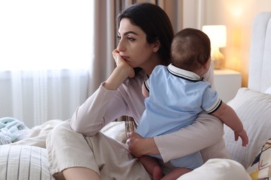 Photo of Woman suffering from postpartum depression with her little baby on bed at home