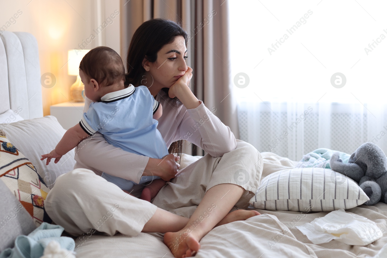 Woman suffering from postpartum depression with her little baby on bed at home. Space for text Photo of Woman suffering from postpartum depression with her little baby on bed at home. Space for text
