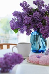 Photo of Bouquet of beautiful lilac flowers, coffee and dessert on white table indoors