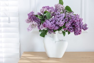 Photo of Bouquet of beautiful lilac flowers on wooden table near white wall