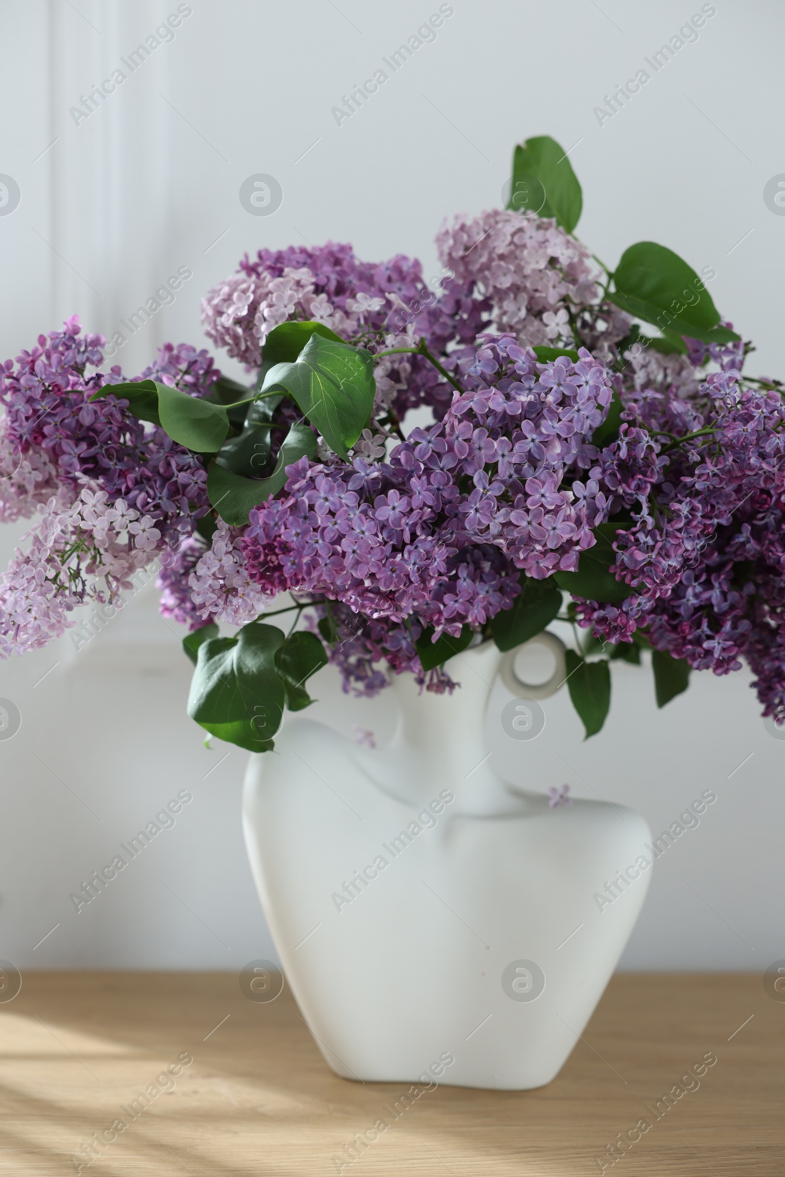 Bouquet of beautiful lilac flowers on wooden table near white wall Photo of Bouquet of beautiful lilac flowers on wooden table near white wall