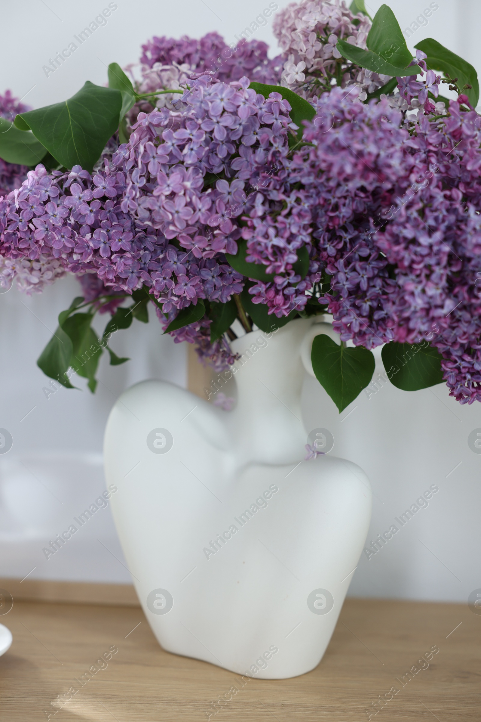 Bouquet of beautiful lilac flowers on wooden table near white wall Photo of Bouquet of beautiful lilac flowers on wooden table near white wall