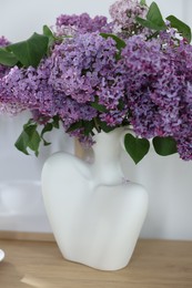Photo of Bouquet of beautiful lilac flowers on wooden table near white wall