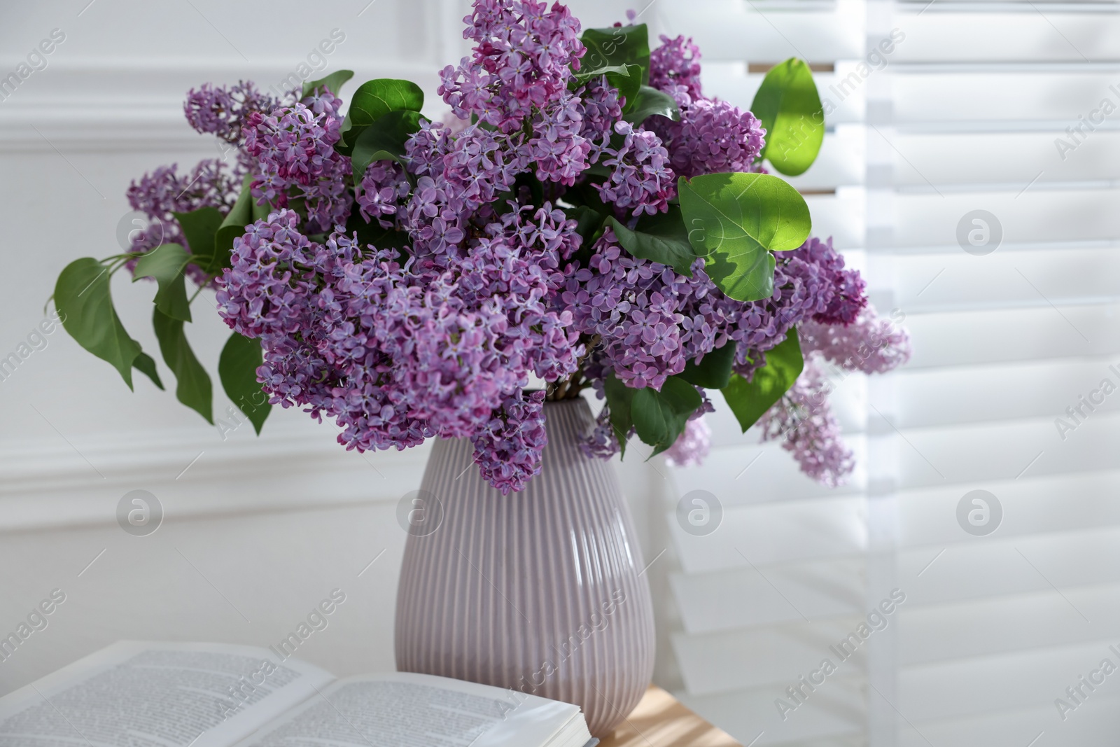 Bouquet of beautiful lilac flowers and book on table indoors Photo of Bouquet of beautiful lilac flowers and book on table indoors