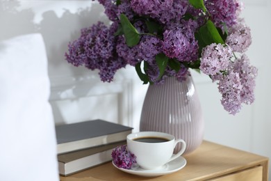 Photo of Bouquet of beautiful lilac flowers, coffee and books on nightstand