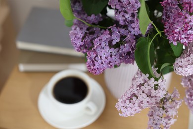 Photo of Bouquet of beautiful lilac flowers and coffee on wooden table, closeup