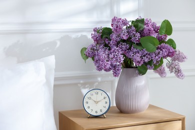 Photo of Bouquet of beautiful lilac flowers and alarm clock on nightstand