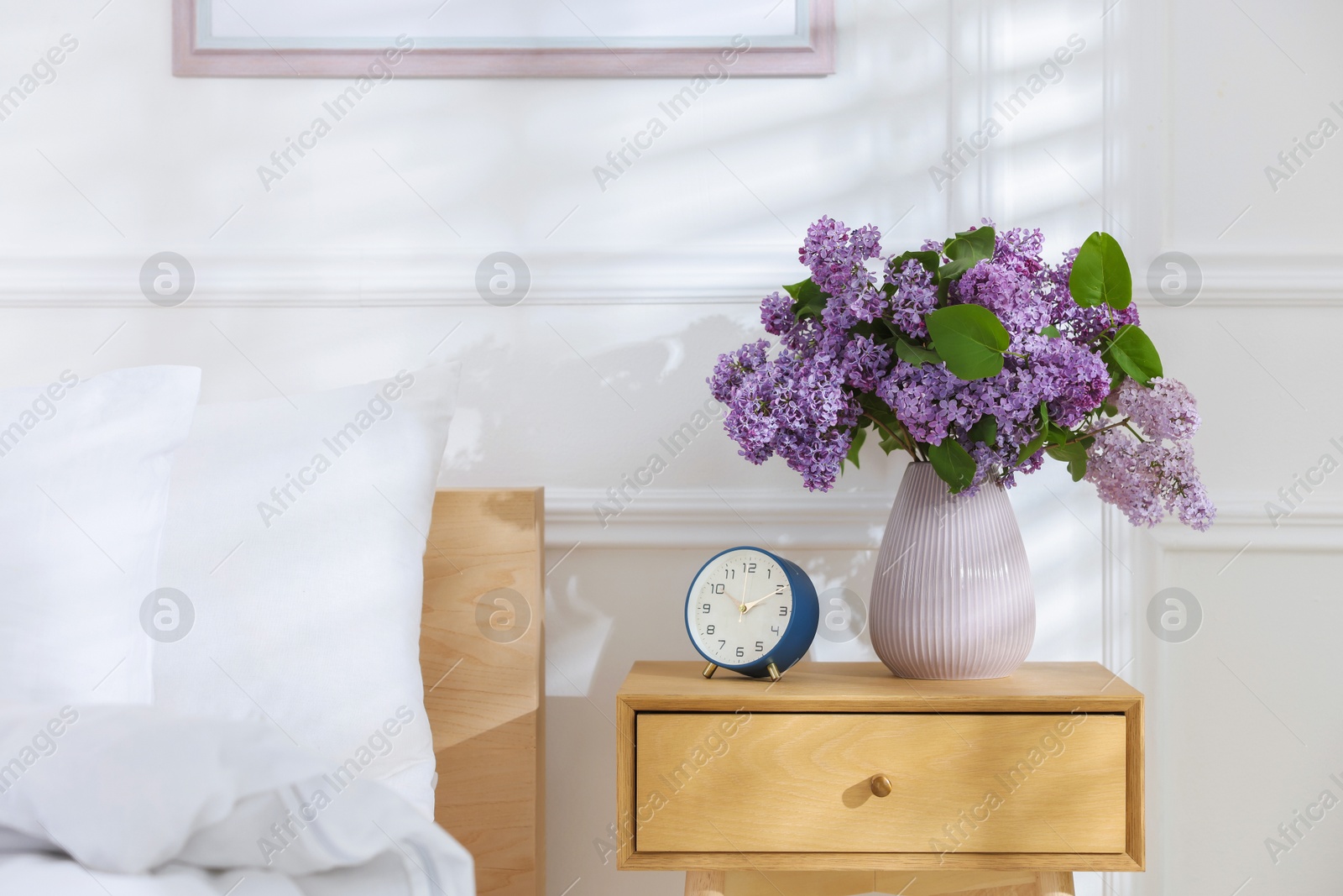 Bouquet of beautiful lilac flowers and alarm clock on nightstand Photo of Bouquet of beautiful lilac flowers and alarm clock on nightstand