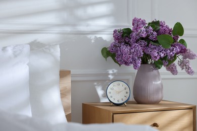Photo of Bouquet of beautiful lilac flowers and alarm clock on nightstand