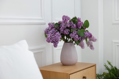 Photo of Bouquet of beautiful lilac flowers on wooden table near white wall