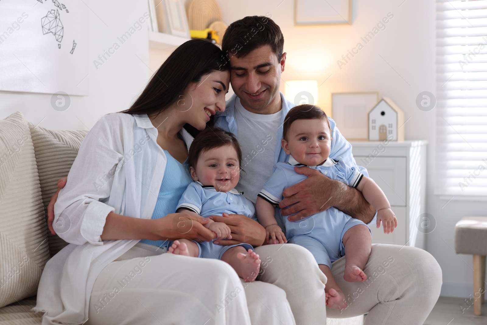 Happy family. Parents with their twin babies on sofa at home Photo of Happy family. Parents with their twin babies on sofa at home