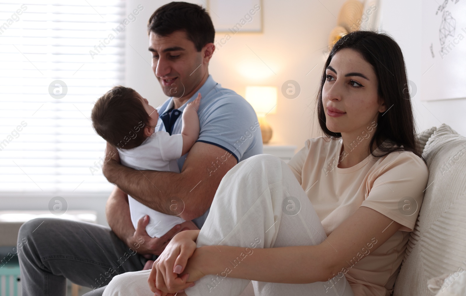 Woman suffering from postpartum depression and her husband with baby on sofa at home Photo of Woman suffering from postpartum depression and her husband with baby on sofa at home