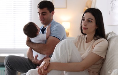 Photo of Woman suffering from postpartum depression and her husband with baby on sofa at home