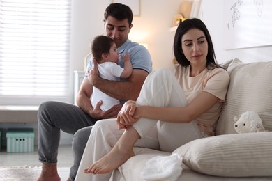 Photo of Woman suffering from postpartum depression and her husband with baby on sofa at home