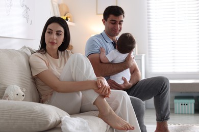 Photo of Woman suffering from postpartum depression and her husband with baby on sofa at home
