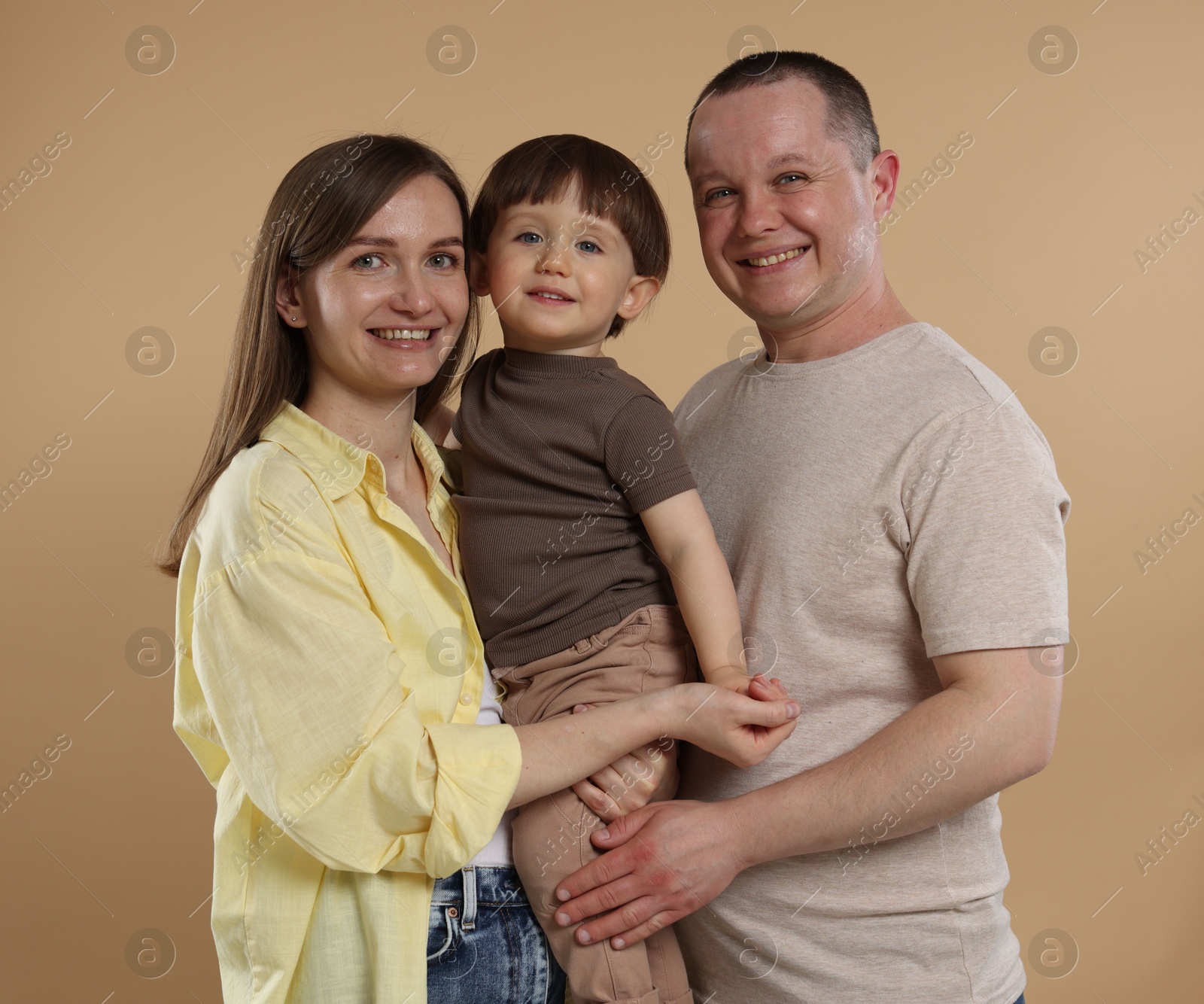 Happy parents and their baby boy on beige background. Lovely family Photo of Happy parents and their baby boy on beige background. Lovely family