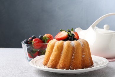 Photo of Tasty Bundt cake with powdered sugar and berries on light grey table, closeup