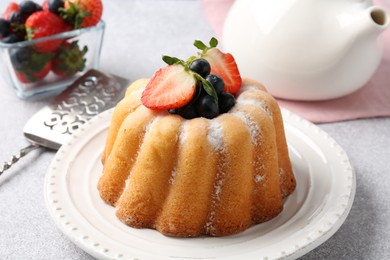 Photo of Tasty Bundt cake with powdered sugar and berries on light grey table, closeup