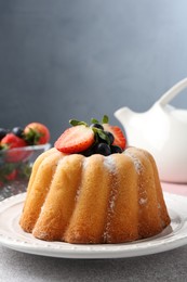 Photo of Tasty Bundt cake with powdered sugar and berries on light grey table, closeup. Space for text