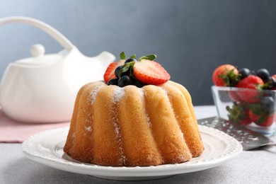 Photo of Tasty Bundt cake with powdered sugar and berries on light grey table, closeup