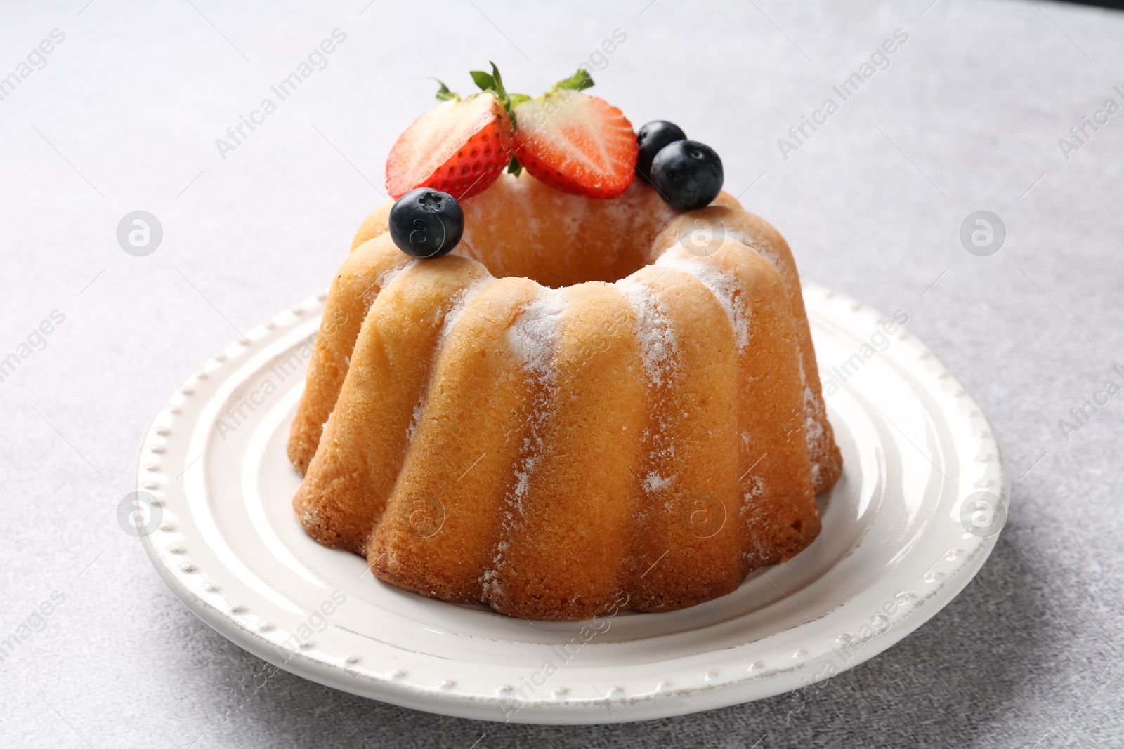 Tasty Bundt cake with powdered sugar and berries on light grey table, closeup Photo of Tasty Bundt cake with powdered sugar and berries on light grey table, closeup