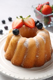 Photo of Tasty Bundt cake with powdered sugar and berries on light grey table, closeup