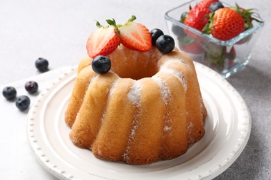 Photo of Tasty Bundt cake with powdered sugar and berries on light grey table, closeup