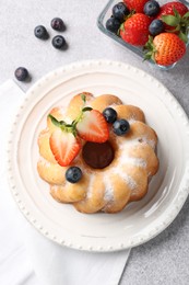 Photo of Tasty Bundt cake with powdered sugar and berries on light grey table, flat lay