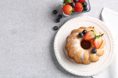 Photo of Tasty Bundt cake with powdered sugar and berries on light grey table, flat lay. Space for text