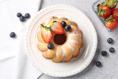 Photo of Tasty Bundt cake with powdered sugar and berries on light grey table, flat lay