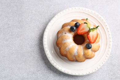 Photo of Tasty Bundt cake with powdered sugar and berries on light grey table, top view. Space for text
