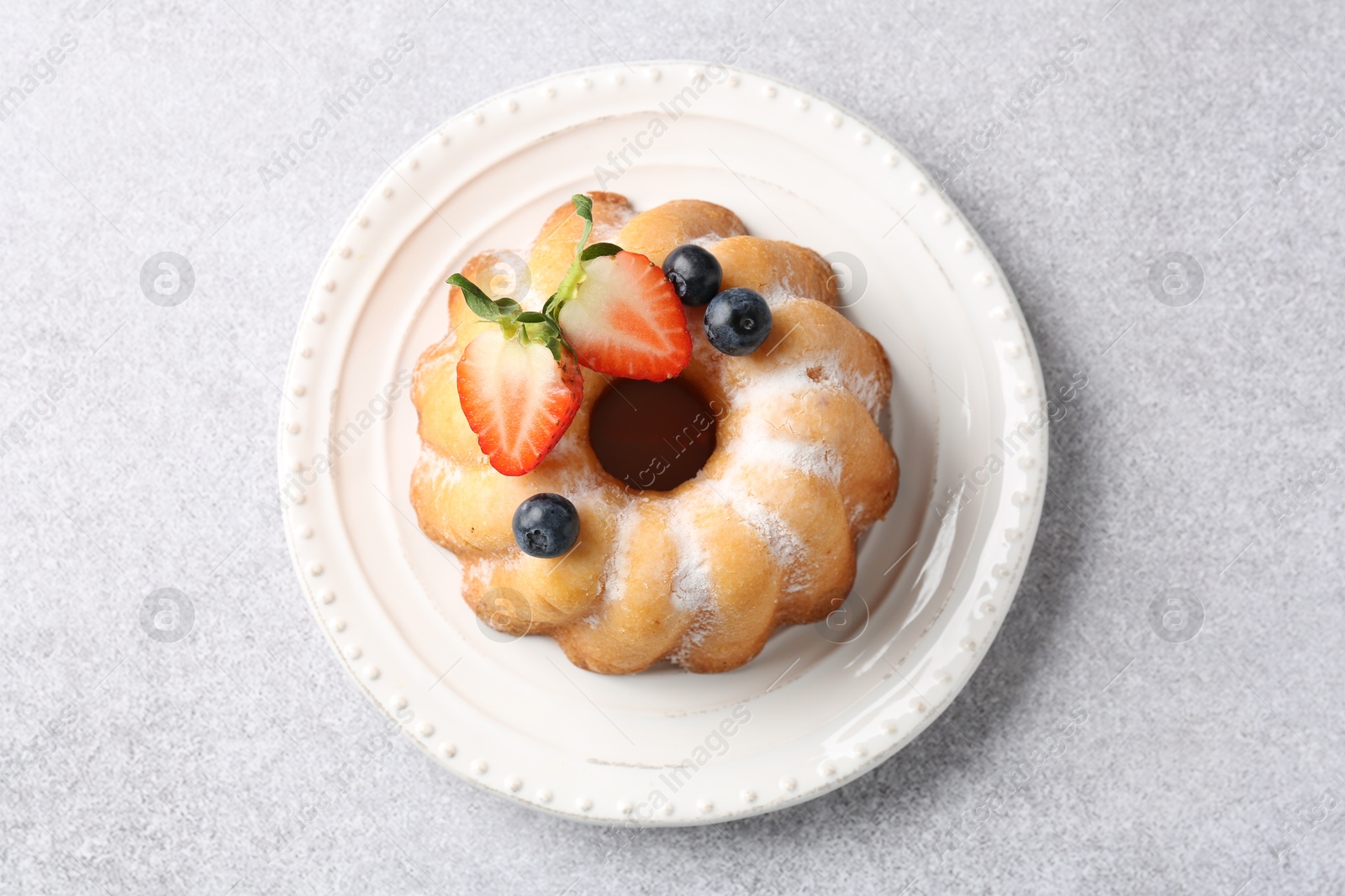 Tasty Bundt cake with powdered sugar and berries on light grey table, top view Photo of Tasty Bundt cake with powdered sugar and berries on light grey table, top view