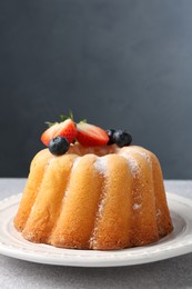 Photo of Tasty Bundt cake with powdered sugar and berries on light grey table, closeup. Space for text