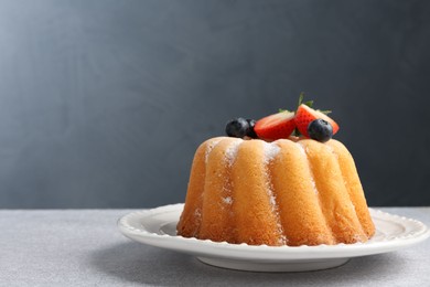 Photo of Tasty Bundt cake with powdered sugar and berries on light grey table, closeup. Space for text
