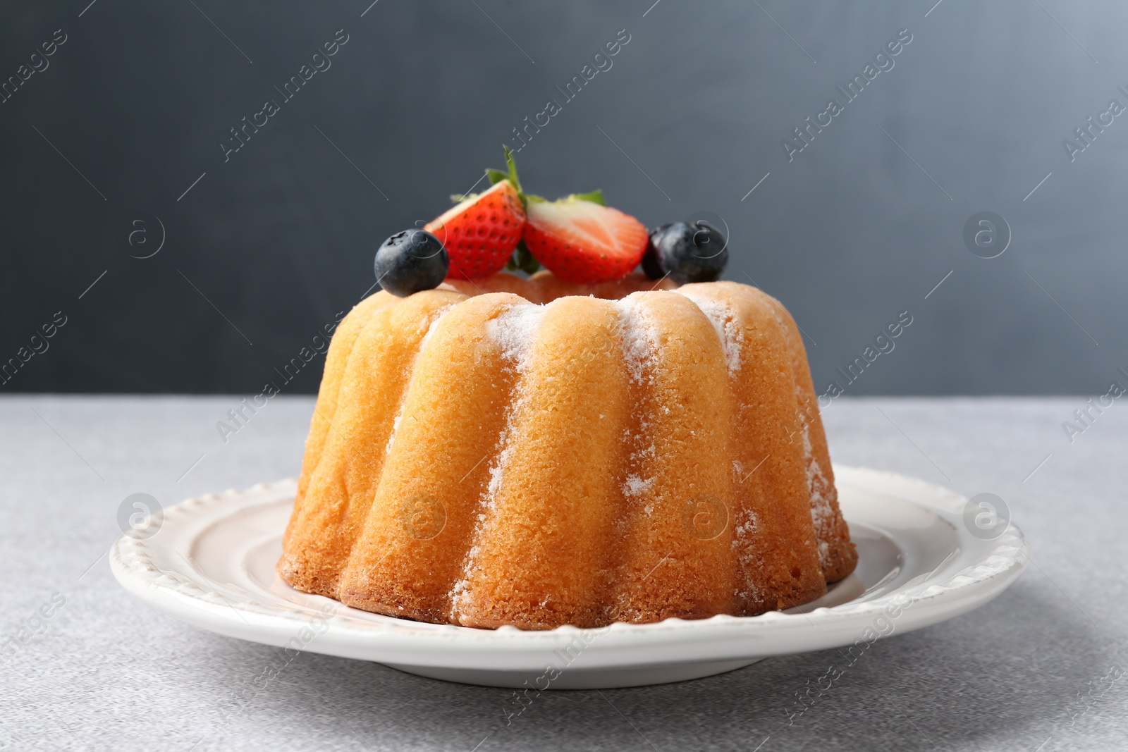 Tasty Bundt cake with powdered sugar and berries on light grey table, closeup Photo of Tasty Bundt cake with powdered sugar and berries on light grey table, closeup