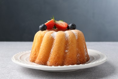 Photo of Tasty Bundt cake with powdered sugar and berries on light grey table, closeup