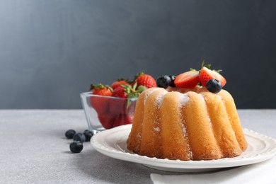 Photo of Tasty Bundt cake with powdered sugar and berries on light grey table, closeup. Space for text